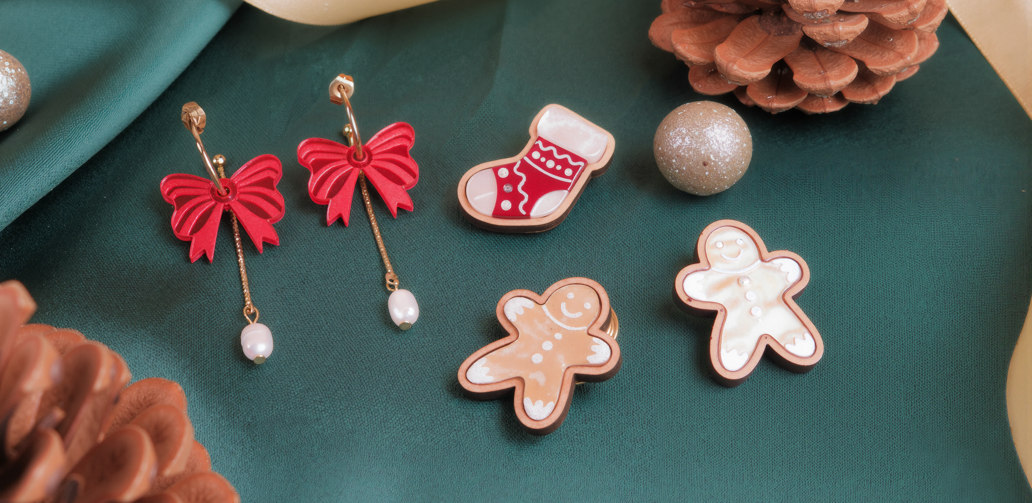 Red bow earrings, Christmas-themed cookies, pinecones, gold ribbon, and glittery ornaments arranged on green satin fabric, creating a festive holiday scene.