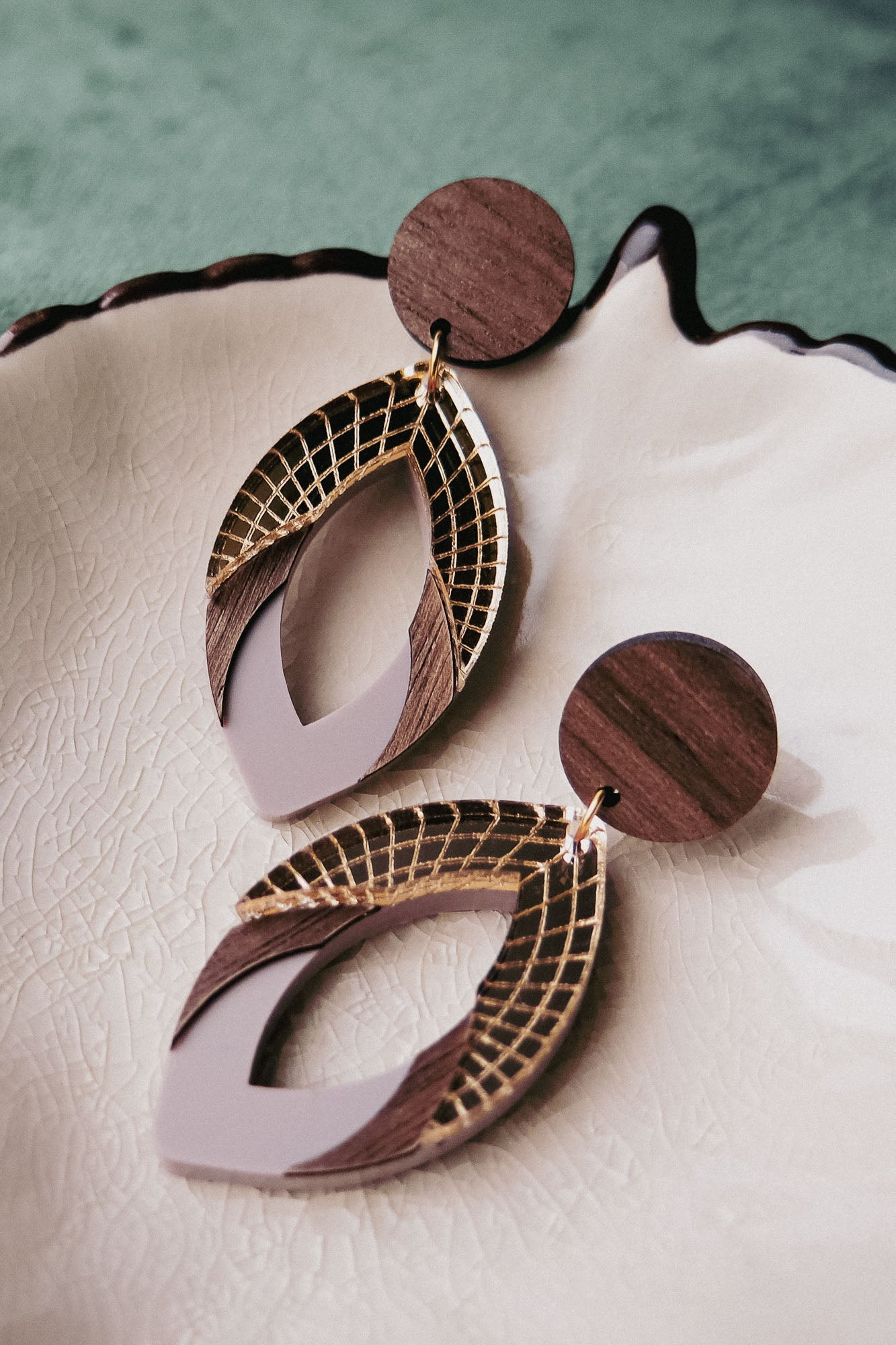 A pair of stylish handcrafted earrings with wooden circular studs and layered geometric dangles featuring gold, brown wood, and light beige accents in premium acrylic glass, displayed on a textured cream-colored dish.