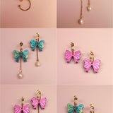 A set of six images shows interchangeable dangle earrings on a pink background: gold-plated c-hoops with freshwater pearls, blue and green bows with pearls, pink bows, green and blue bows, and mixed pairs with bows and pearls.