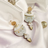 A pair of decorative Poinsettia Statement Hoops with gold, white, and silver details are displayed on white satin fabric, accompanied by glittery gold spheres—perfect as festive earrings to elevate your holiday jewelry collection.