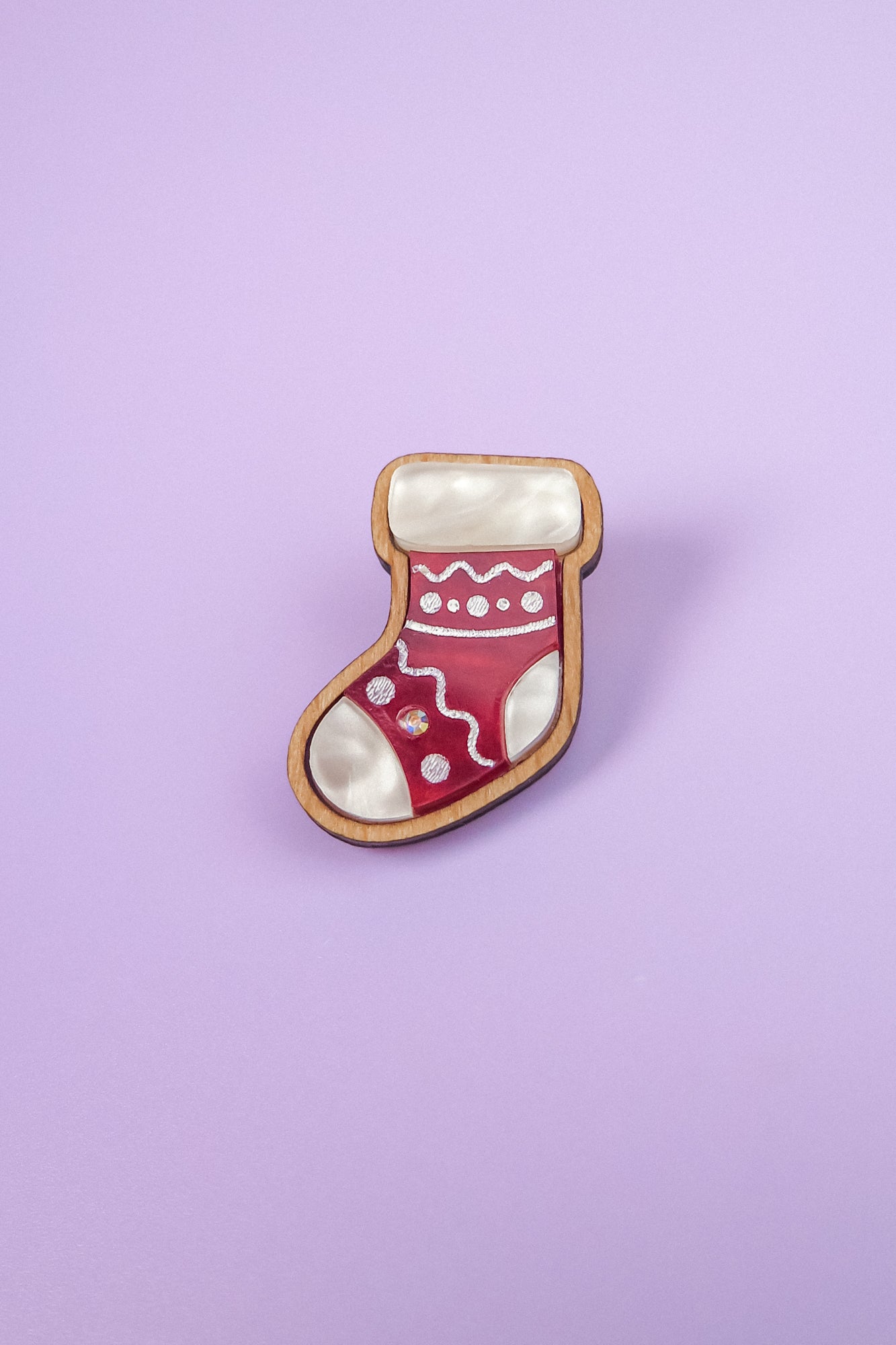 This handcrafted Christmas Stocking Pin, featuring red, white, and wood-tone details, is displayed against a light purple background—perfect for adding festive charm to your holiday wardrobe.