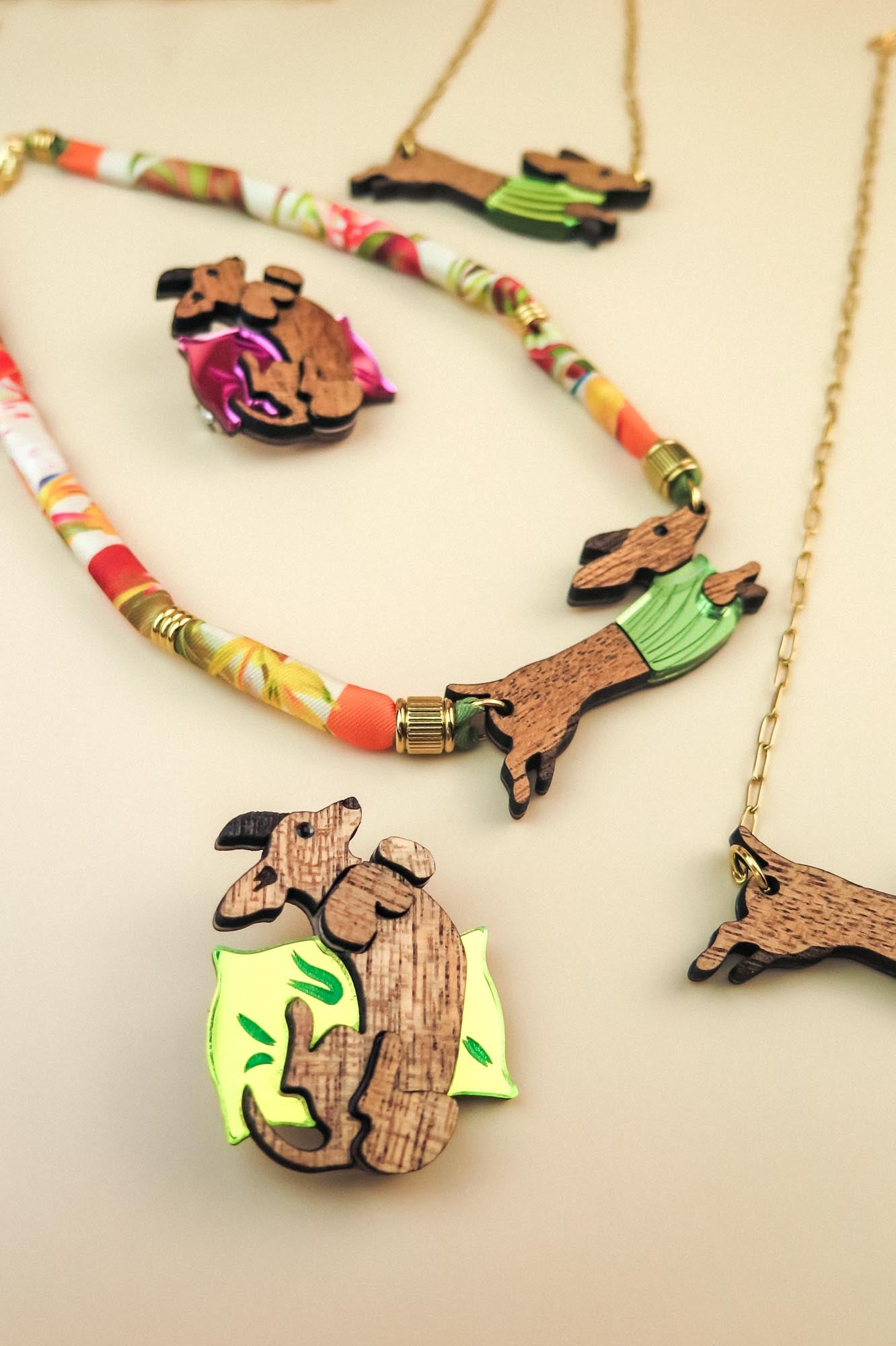 Assorted jewelry pieces featuring dachshund dog designs made of wood and colorful materials, including a playful brooch, necklaces, and unique dog accessories, displayed on a light beige surface.