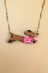 Gold chain necklace with a pendant shaped like a brown Dachshund dog, wearing a colorful sweater and crafted from sustainable wood, set against a beige background.