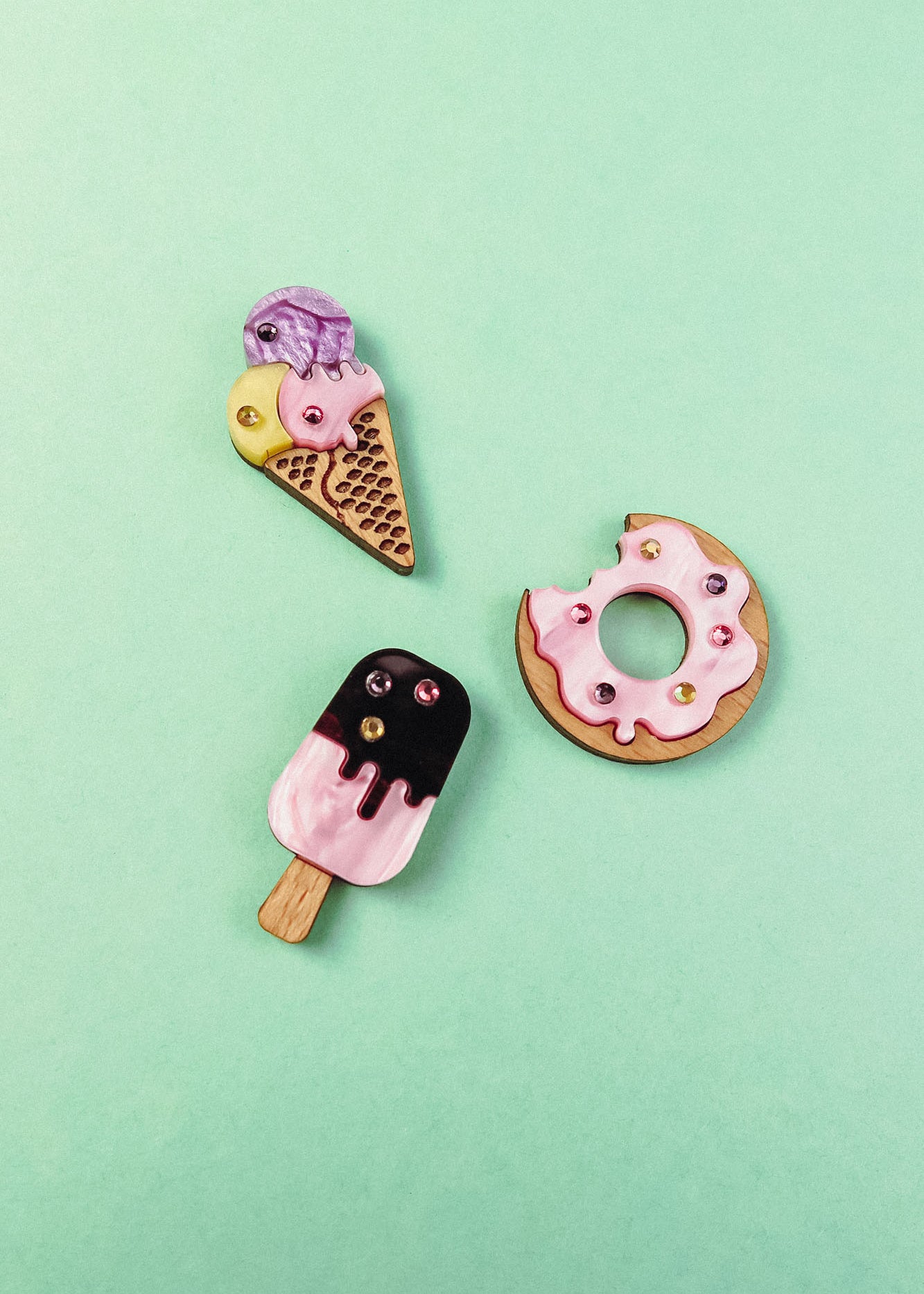 Three handcrafted clay pins on a mint green background: an ice cream cone, a Donut Pin with colorful rhinestones and sprinkles, and a pink-and-black popsicle.