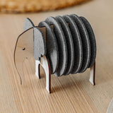 A set of round, gray Elephant Coasters is stacked vertically in a wooden holder shaped like an elephant, adding witty design and furniture protection to your light wood table.