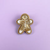 A Gingerbread Man Pin brooch with a smiling face and decorative white icing details, set against a solid light purple background—perfect for adding a festive touch to your Christmas party outfit.