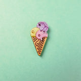 A handcrafted Ice Cream Pin with a playful design features three whimsical scoops—yellow, pink, and purple—on a light green background.