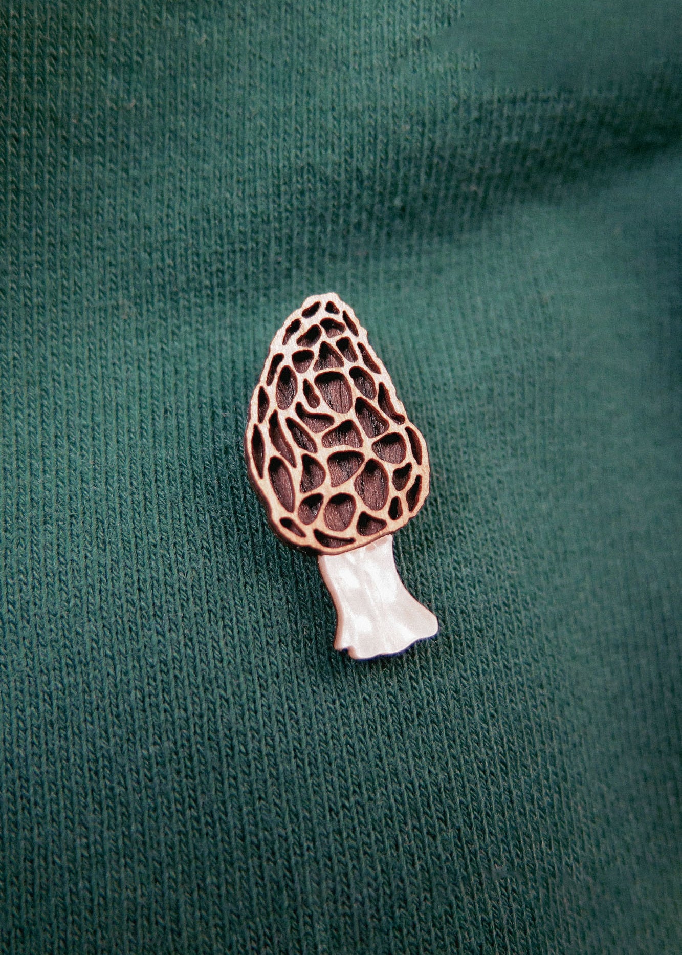 A handcrafted Morel Mushroom Pin is attached to a green, ribbed fabric, likely on a shirt or sweater.