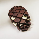 A sustainable Pinecone Brooch, crafted from recycled wood with gold accents, sits on a white surface, casting a soft shadow.