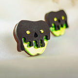 Two handcrafted cookies shaped like skulls with black tops and neon green dripping icing, featuring yellow eyes and nose holes, deliver a unique Halloween look as they rest on a light fabric surface.