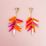 Gold dangle earrings with dangling pink, orange, and gold leaf-shaped charms arranged in layers, these featherlight earrings are displayed on a pale pink background.