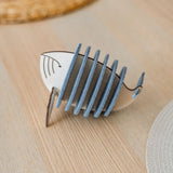 A wooden and felt Whale Coasters holder shaped like a stylized fish adds home charm as it sits on a light wooden table, protecting surfaces with woven placemats in the background.
